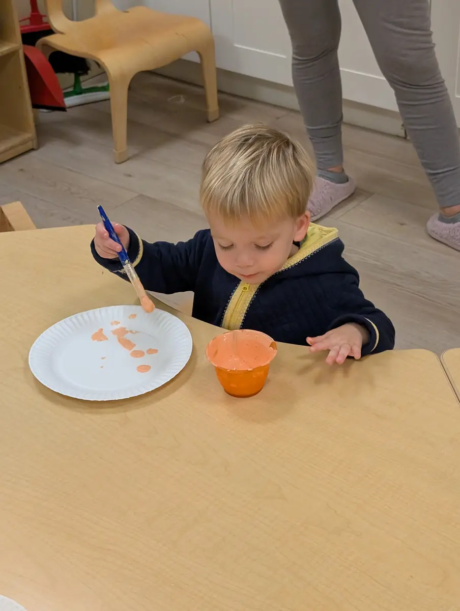 A toddler painting with a brush at the art table at Blossom Station in Acton, MA