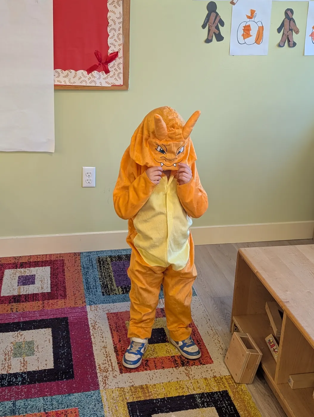 A toddler in an orange dragon costume in a Blossom Station classroom on Halloween 2026