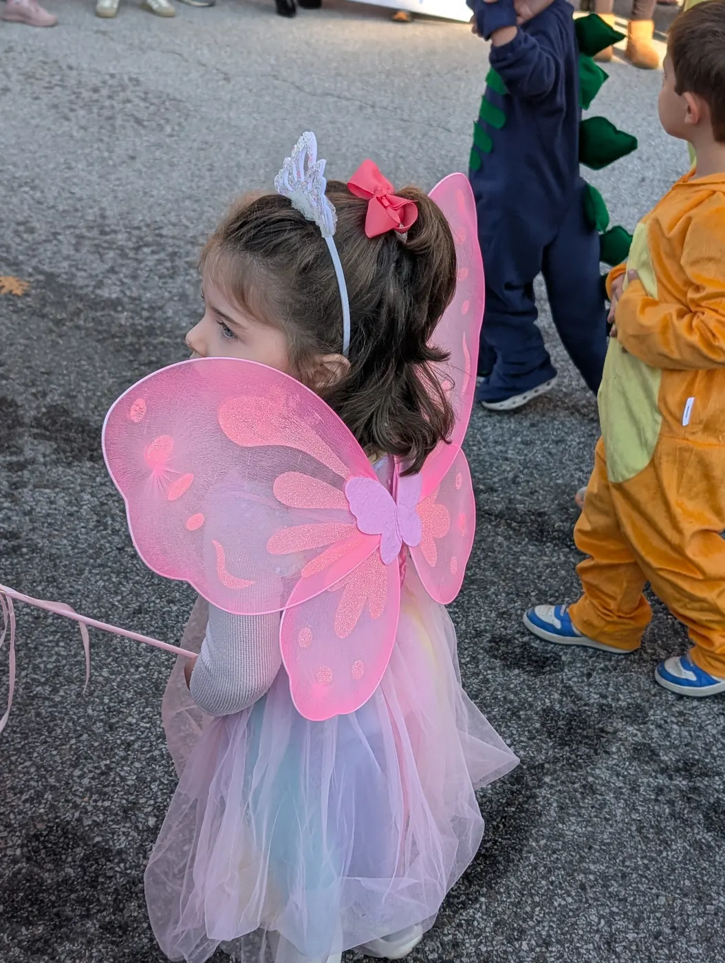 A toddler with pink butterfly wings and a bow headband at the 2026 Halloween Parade