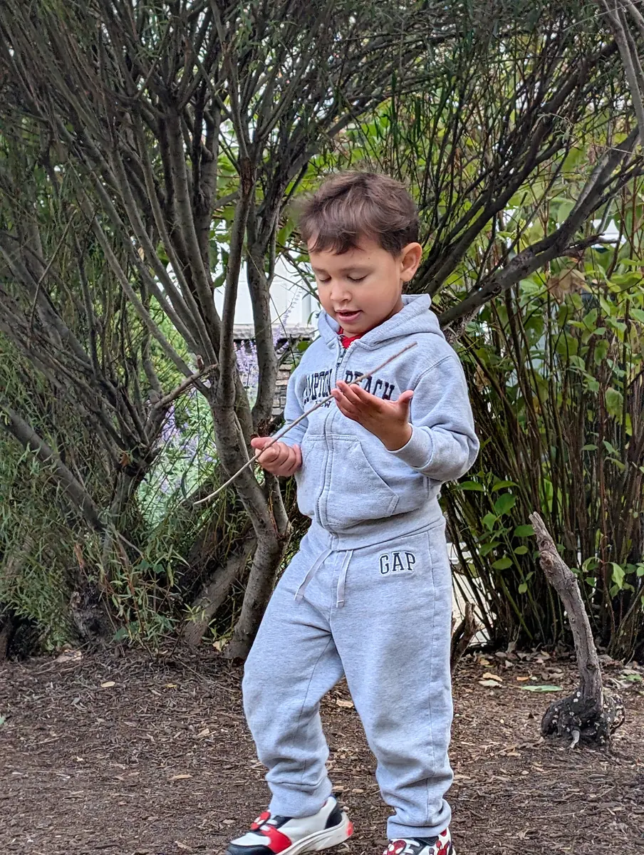 A preschooler examining a stick and exploring nature outdoors with Blossom Station