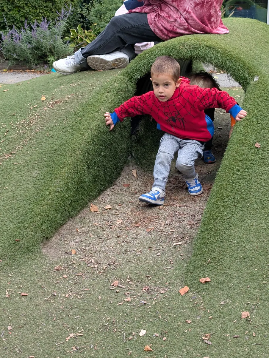 A child crawling through a grass tunnel during outdoor TimberNook play with Blossom Station in Acton, MA