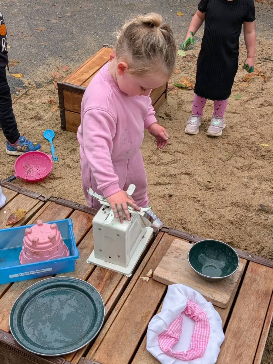 A preschooler weighing apples on an old kitchen scale at the TimberNook pretend shop at Blossom Station
